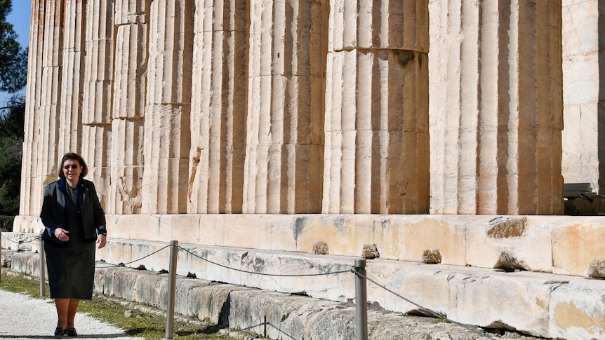 Lina Mendoni walks next to a Greek temple. 