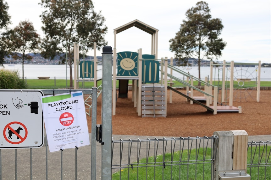 Playground equipment behind a fence which has a sign that says "playground closed" attached to it