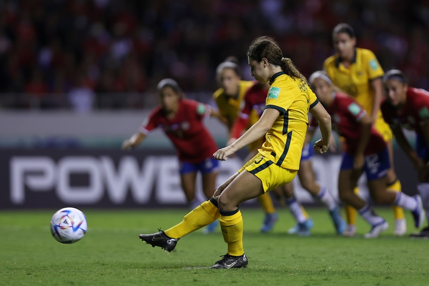 A female soccer player wearing yellow and green kicks a ball