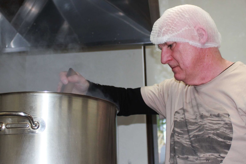 A male volunteer stirs soup in a large pot on the stove.