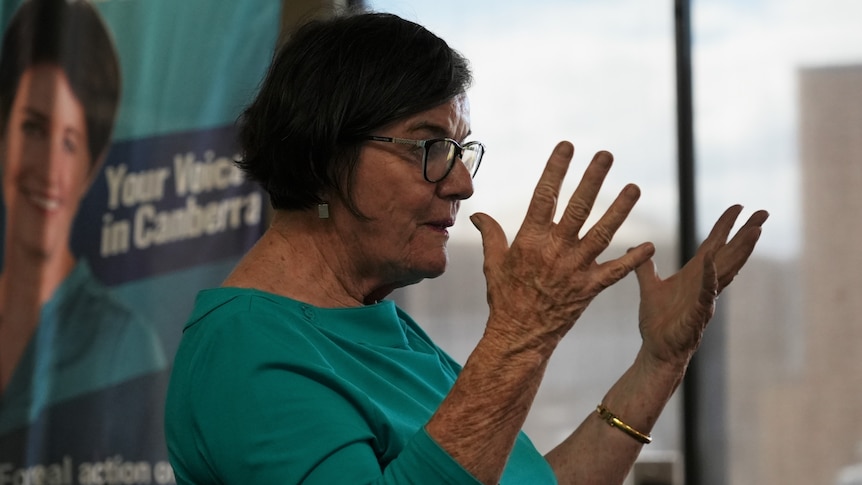 Cathy McGowan wears a teal coloured shirt while gesturing with her hands 
