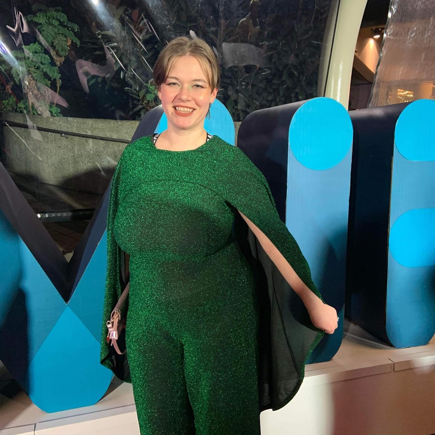 Silvi Vann-Wall dressed-up at an event in a shimmering green pantsuit with a built-in cape