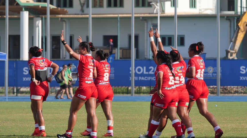 A group of women wearing red jerseys walk off a field together, waving at supporters.