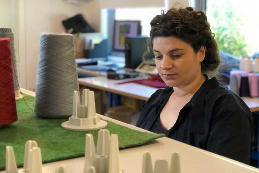 cones of yarn are in the foreground, while Patricia stares down into the knitting machine behind them