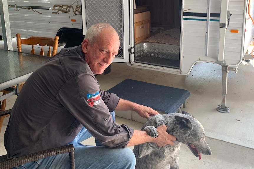 Trevor Abela and his blue heeler sit outside his caravan.