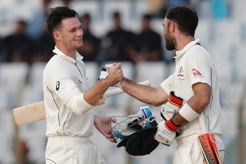 Batsmen Peter Handscomb, left, and Glenn Maxwell shake hands in the middle of the pitch with their helmets off.