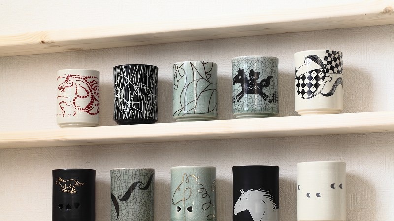 A collection of eight cups on a shelf.