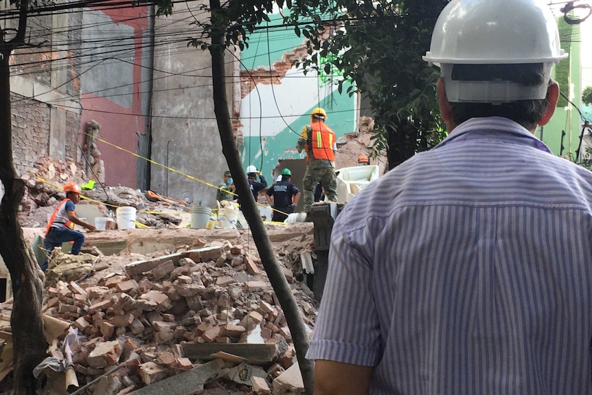 A rescue worker watches on as their colleagues search through the rubble of a Mexico City building.