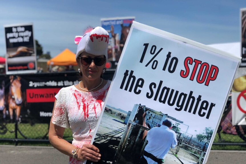 A protester at the Melbourne Cup with a sign and a bloodied costume.