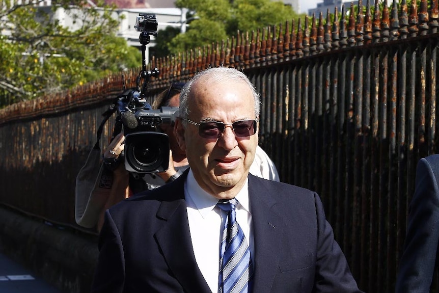 Upper body photo of Eddie Obeid arriving at the Supreme Court, followed by a TV camerman.