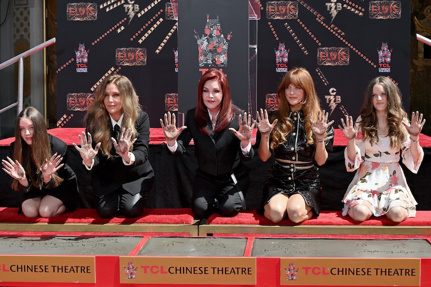 Vivienne Ann Lockwood, Lisa Marie Presley, Priscilla Presley, Riley Keough, and Finley Aaron Love Lockwood kneel.