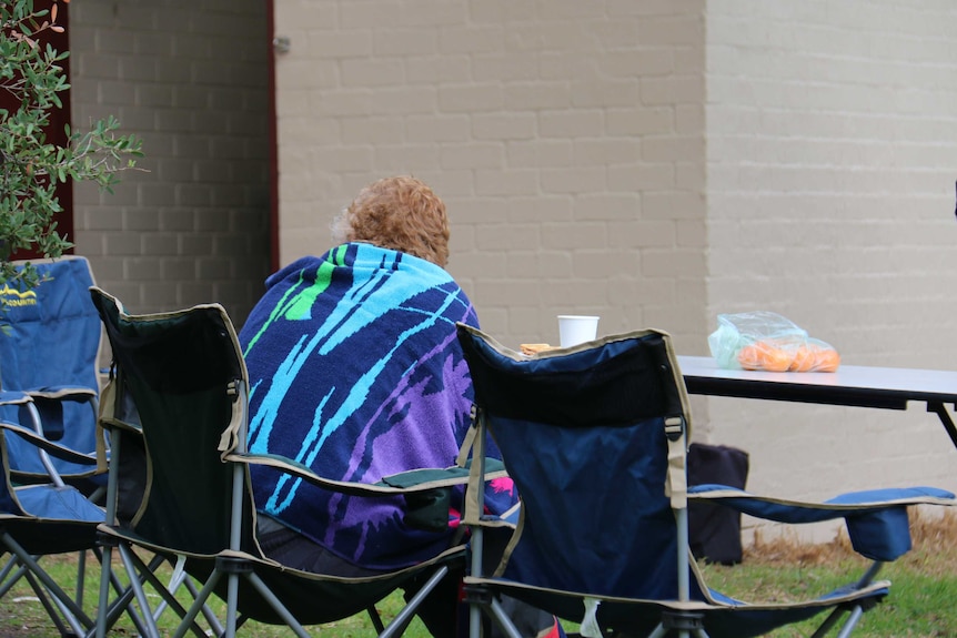 A homeless woman sitting at a table wrapped in a towel on the Mornington Peninsula, Victoria.