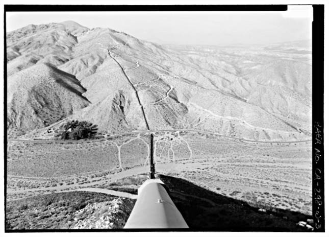 Black and white image of a big pipe going up and through mountain ranges