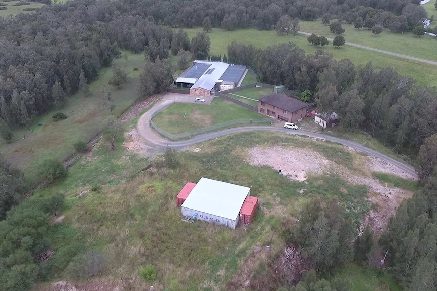 Wide aerial shot of a property from a drone including a flood mound, shipping container, house and boarding kennel.