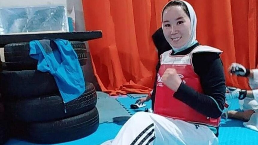 Zakia Khudadadi sits on the floor wearing taekwondo kit, clenching her fist and smiling