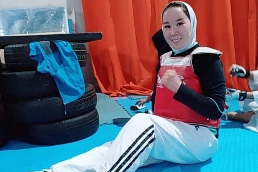 Zakia Khudadadi sits on the floor wearing taekwondo kit, clenching her fist and smiling