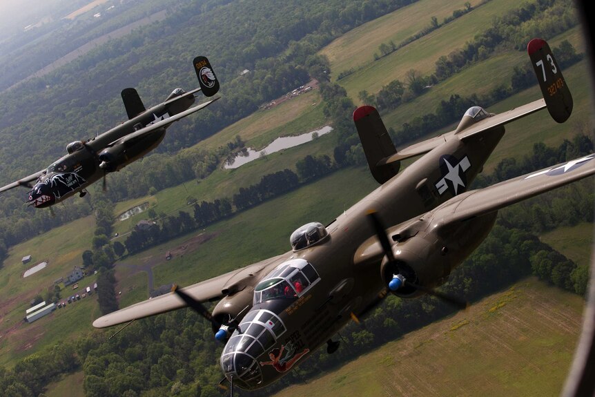 Two B-25 Mitchell bombers fly in formation with dozens of other World War II era aircraft