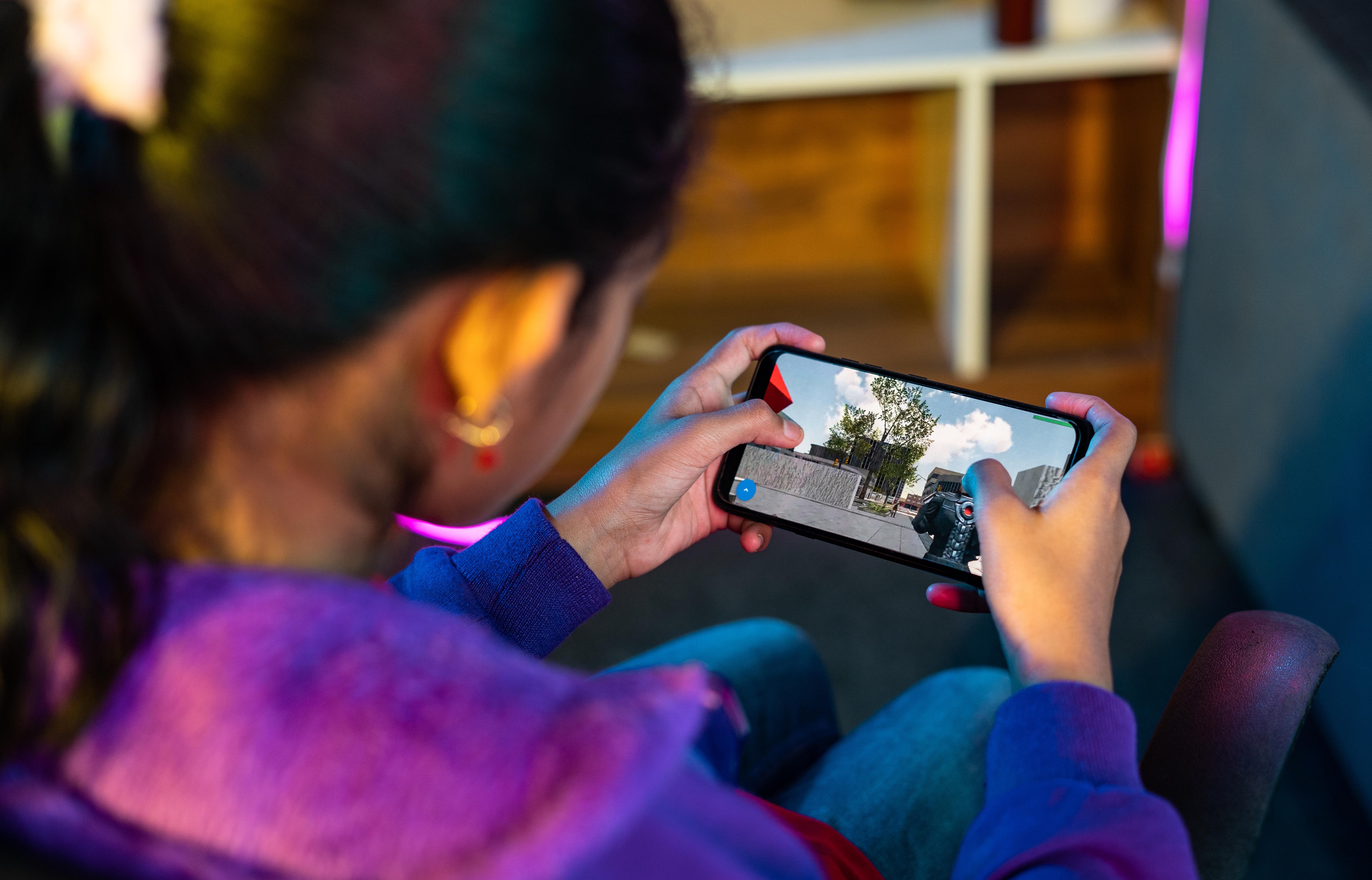 An over-the-shoulder image of a girl playing a game on a smartphone.