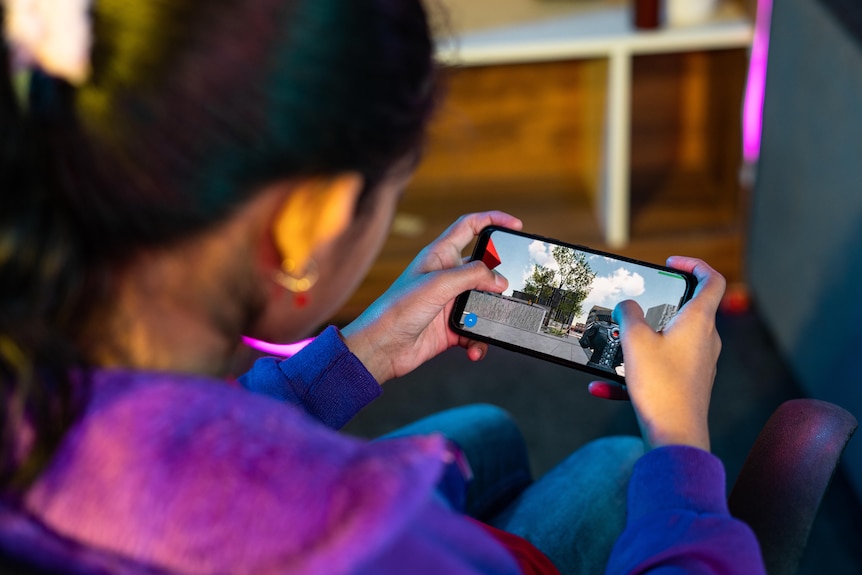An over-the-shoulder image of a girl playing a game on a smartphone.