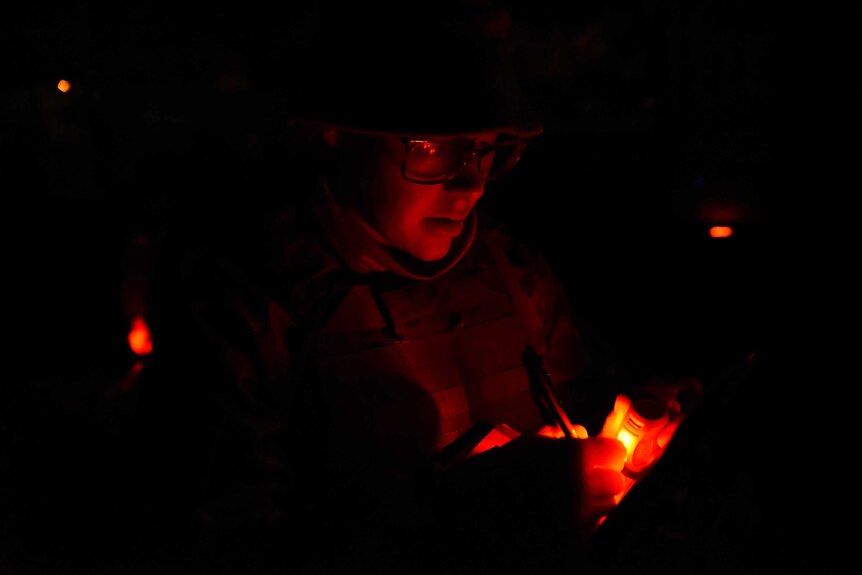 A soldier writes under red torchlight during Exercise Hamel