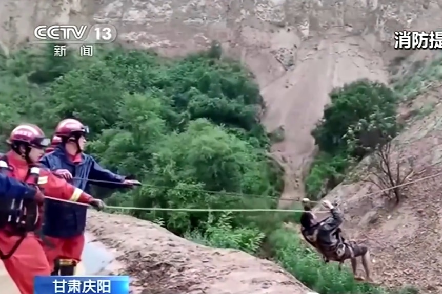Emergency personnel use ropes to pull a worker to safety after landslides in a mountainous area.
