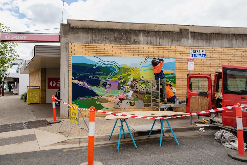 A worker drills the boards the mural is painted on to the wall of a post office.