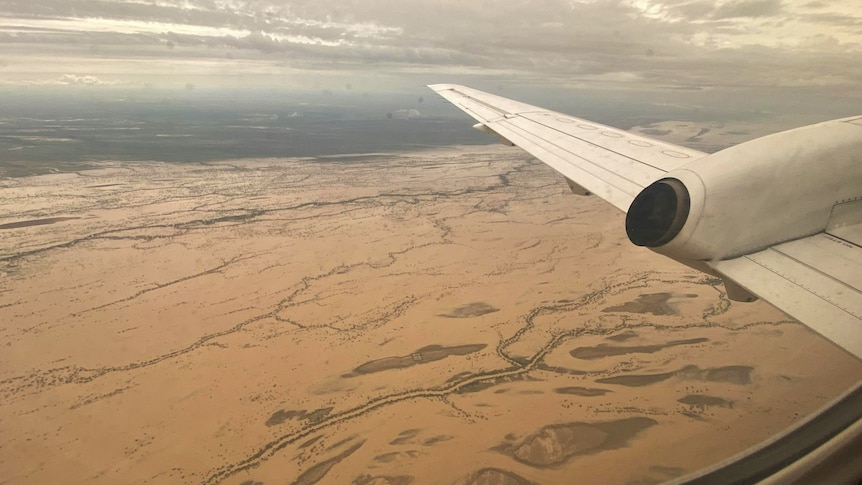 a white plane flies over an enormous mass of brown water in the most remote part of outback Queensland