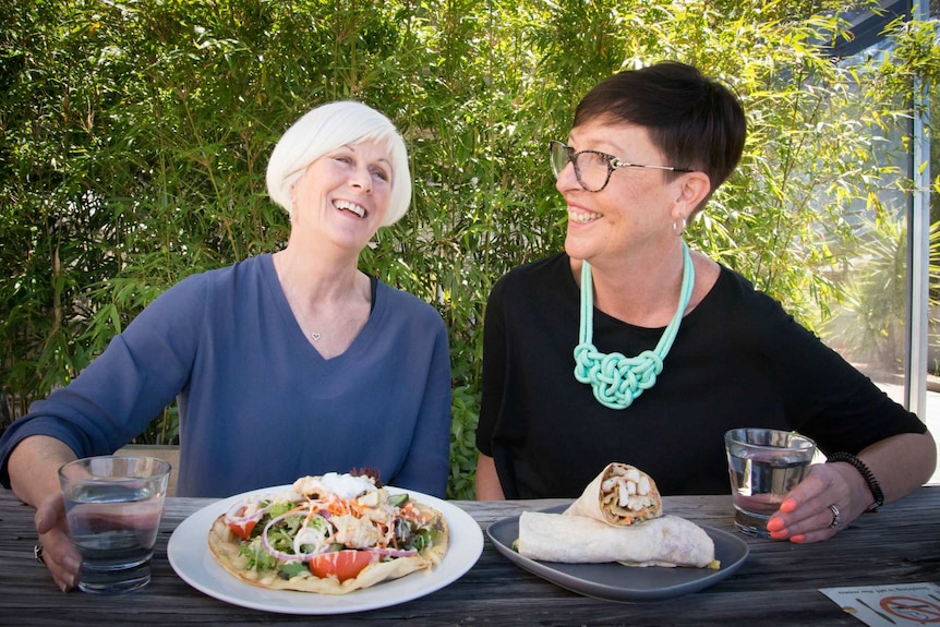 Two women laugh while sharing a meal at an outdoor table at a Warracknabeal pub.