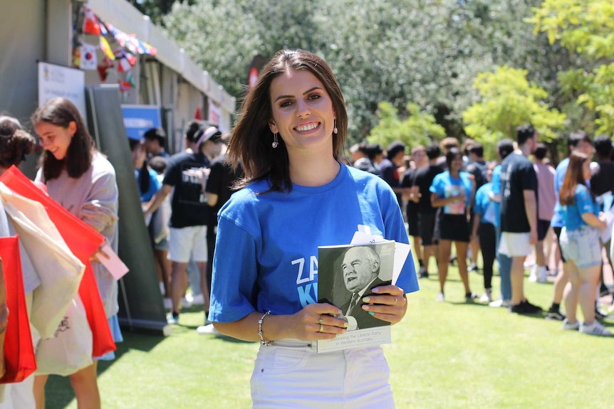 young woman in blue Liberal campaign shirt holding brochure and standing in front of crowd