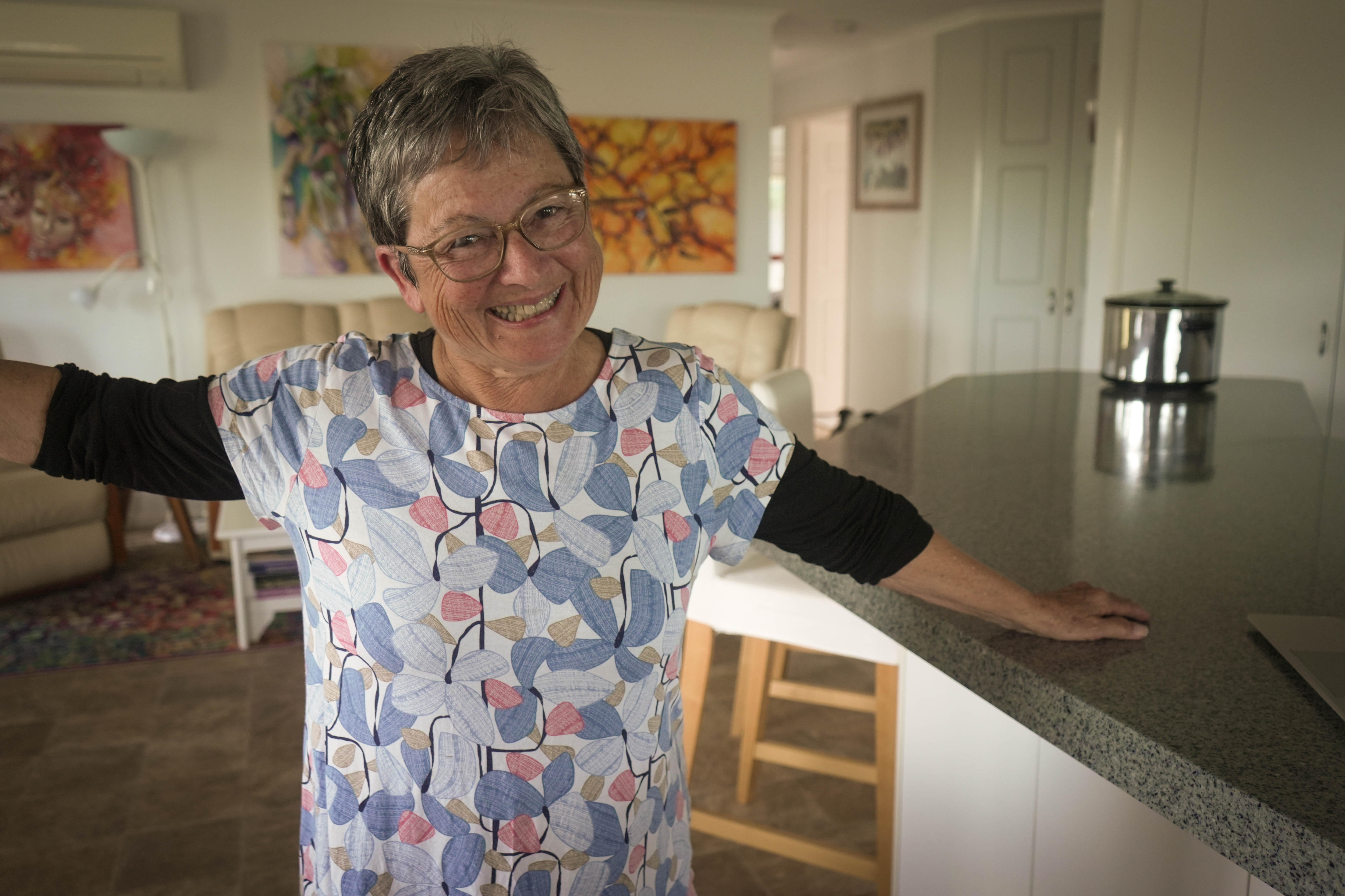 A woman raises her arm while standing next to a kitchen bench