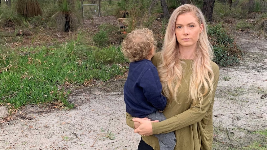 Lauren Dry in an olive green top, holding her child on her hip in a bush setting.