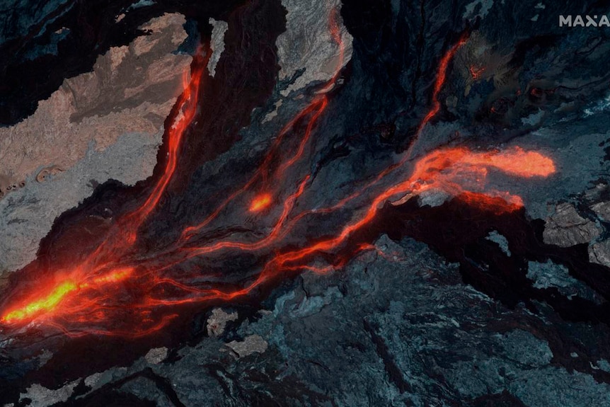 Aerial image shows streams of yellow and red lava flowing over a dark surface