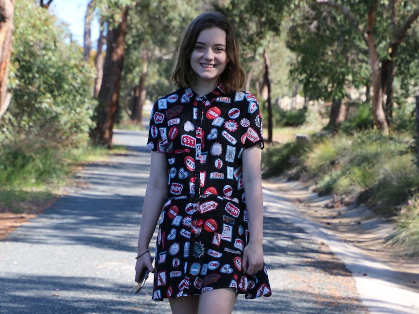 Charlotte stands on a path with trees in the background.