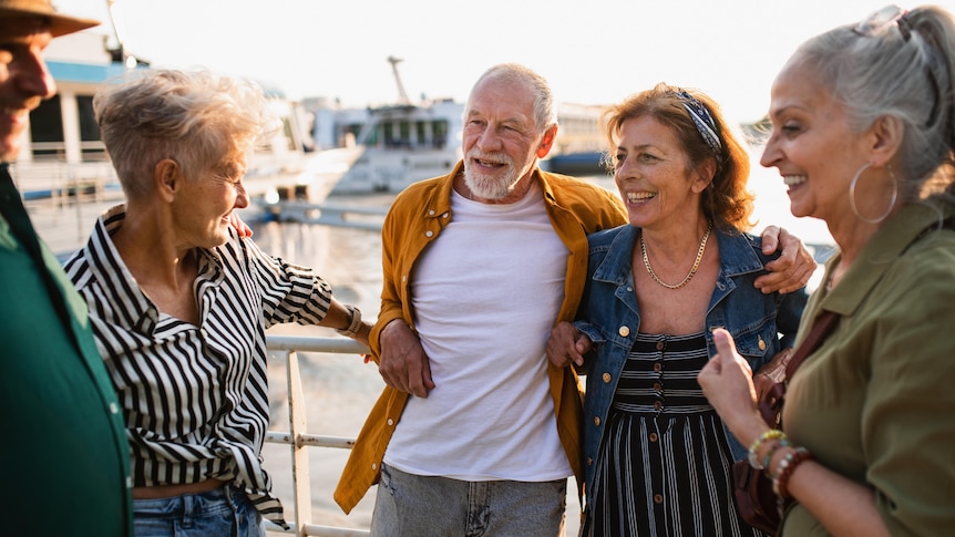 Five seniors stand in a group smiling on a marina port in front of boats