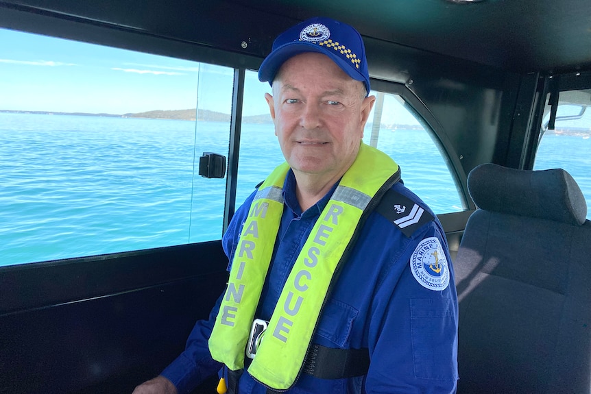 A man in uniform steering a boat with a body of water in window