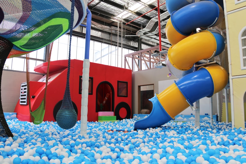 A playground with a red truck, blue and yellow slide and blue ball pit 
