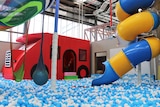 A playground with a red truck, blue and yellow slide and blue ball pit 