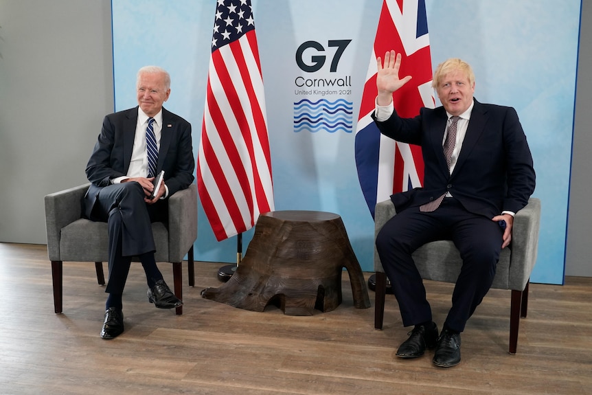 President Joe Biden sits down next to British Prime Minister Boris Johnson as he waves his hand.