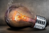 A lightbulb sits on a flat surface, glowing orange and emitting smoke.