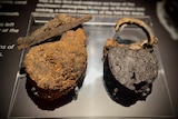 A rusted black and brown metal padlock, next to the concrete layer it was excavated from. 
