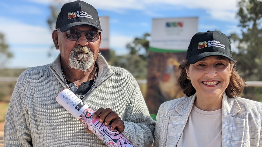 An older Aboriginal man stands next to a smiling woman.