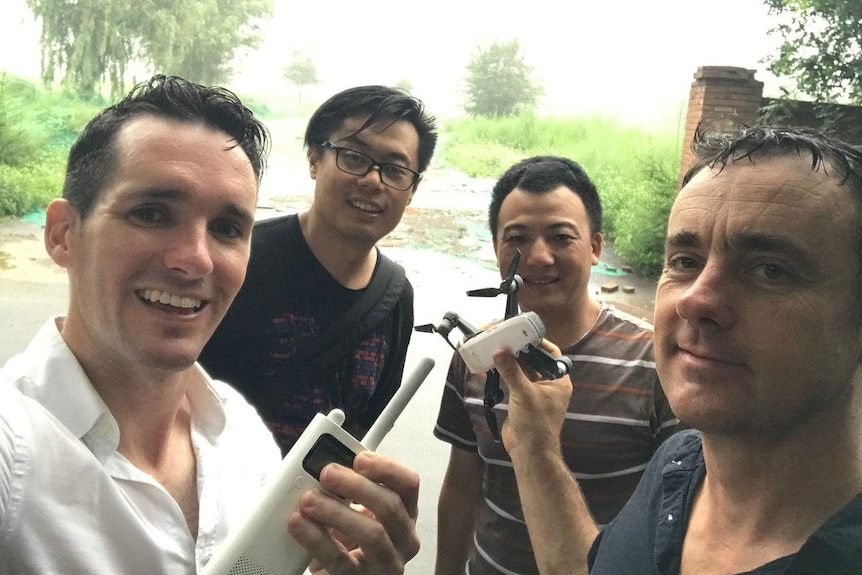 Four smiling at camera holding drone and controller.