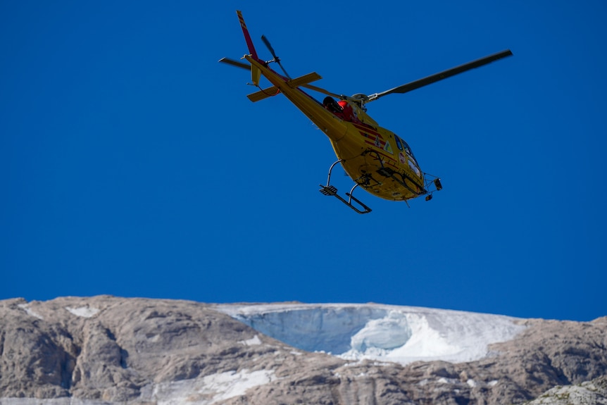 Helicopter flies over snow on mountain 