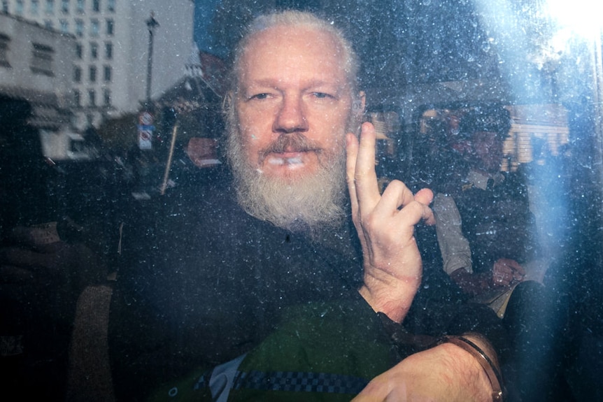Julian Assange gives the peace gesture to the media from a police vehicle at Westminster Magistrates court, April 11, 2019. UK