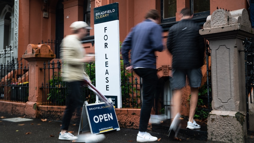 People walk through the front door of a house, past a For Lease sign.