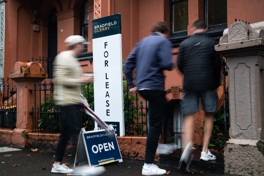 People walk through the front door of a house, past a For Lease sign.