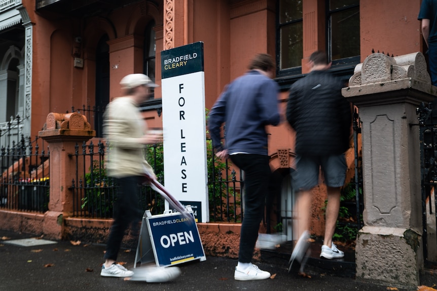 People walk through the front door of a house, past a For Lease sign.