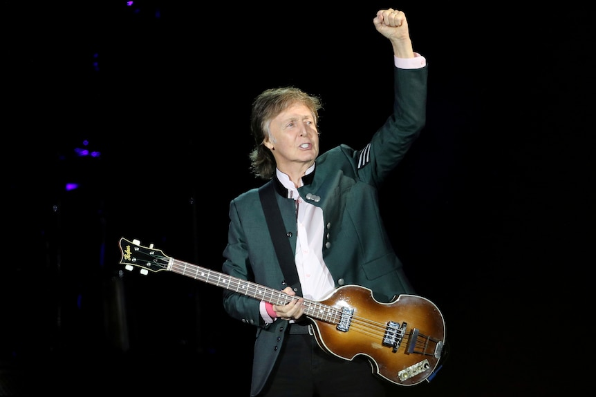 Paul McCartney plays the guitar on stage.