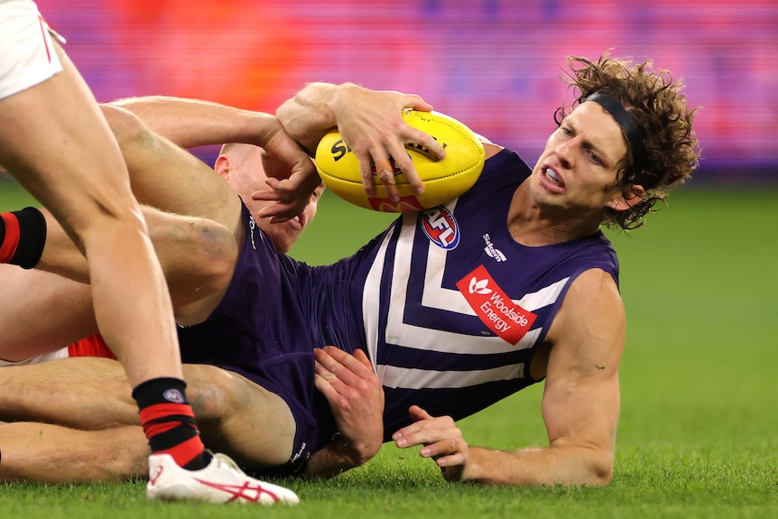 Fremantle Dockers player Nat Fyfe holds the ball while being tackled on the ground. 