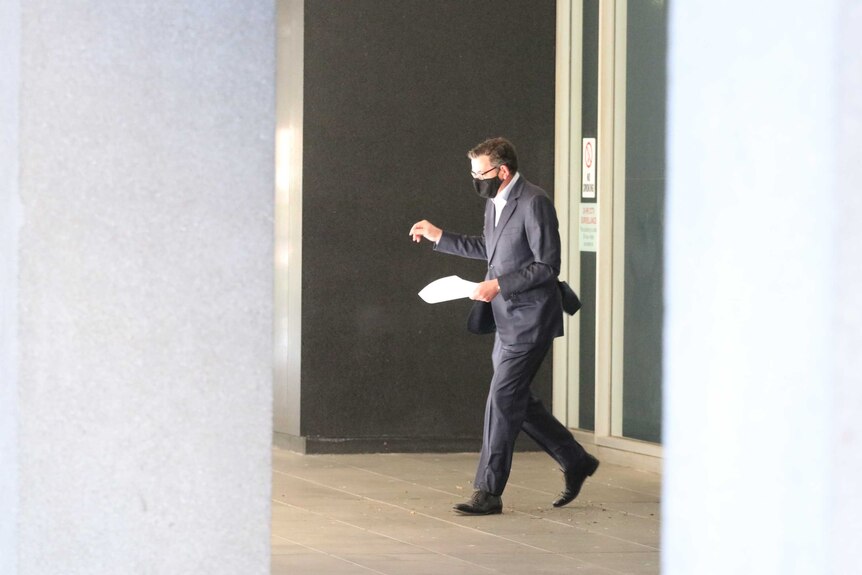 Daniel Andrews walking with a sheet of paper in a suit and mask to a press conference.